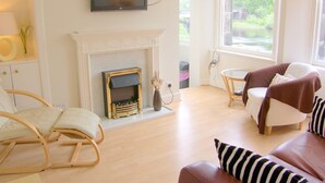 Un salon doté d’une cheminée, d’un téléviseur fixé au-dessus, d’un canapé avec des coussins à rayures et d’un fauteuil avec un coussin.