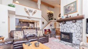 A spacious living room with a leather sofa, a stone fireplace, and a dining area in the background. - Snowcreek #856 Phase V (Mammoth Lakes)