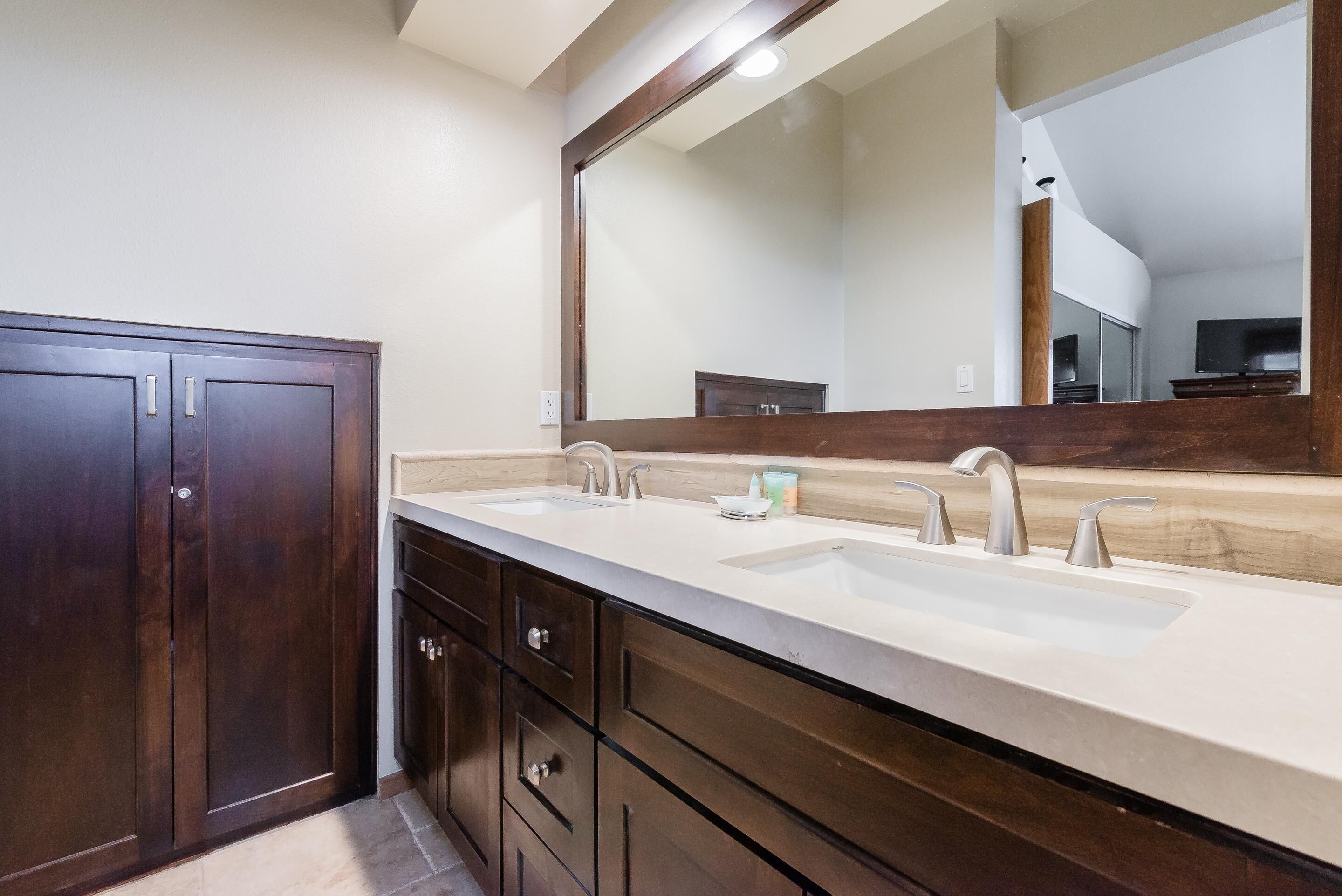 A bathroom with a double sink vanity, dark wood cabinets, and a large mirror.