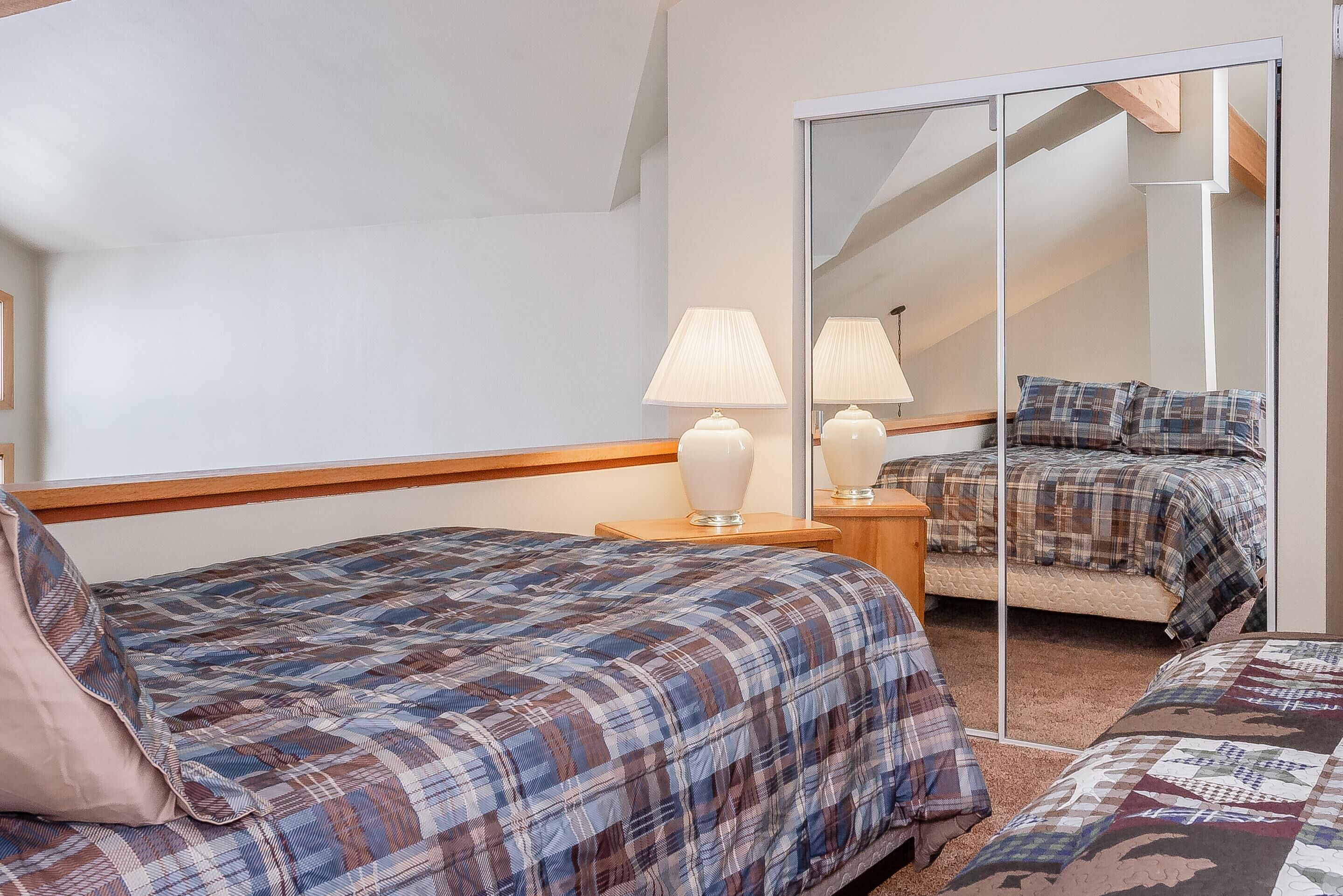 A bedroom with two beds, a mirror, and a nightstand with lamps.