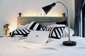 Ein ordentlich bezogenes Bett mit einem Laptop, Kissen und einer Nachttischlampe.