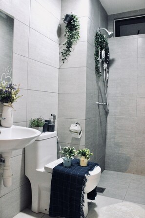 Ein modernes Badezimmer mit einem weißen Waschbecken, einer Toilette und einer Dusche. Auf der Toilette und im Duschbereich stehen Blumentöpfe.