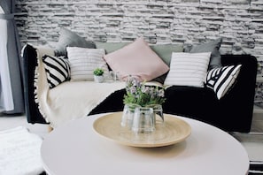 Una sala de estar moderna con pared de piedra, sofá a rayas blanco y negro, y una mesa de centro redonda con un jarrón de flores.