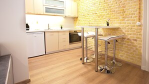 A modern kitchen with wooden flooring, white cabinets, a stainless steel sink, and a brick wall. - Liston Suite Plaza (Corfu)