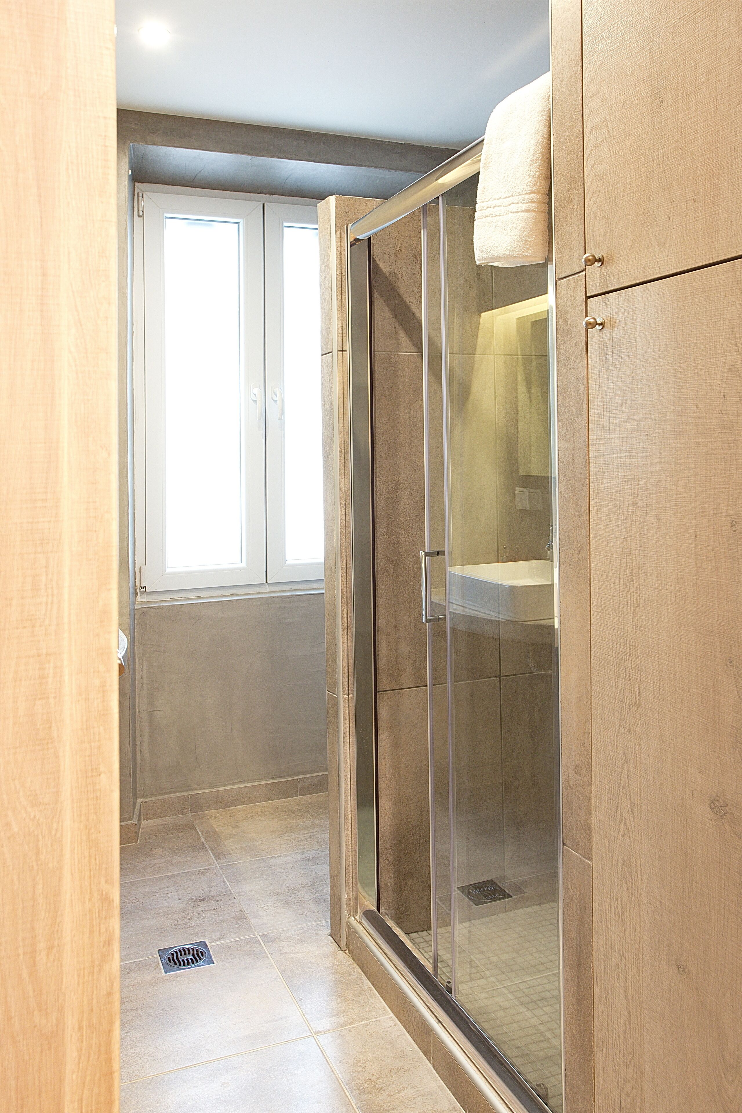 A modern bathroom with a glass shower enclosure, a visible toilet, and a window providing natural light.