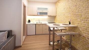 A compact kitchen with a wooden floor, a dining table with stools, and a brick wall.