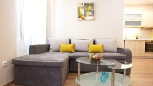 A modern living room with a grey sectional sofa, two yellow cushions, and a glass coffee table. - Liston Suite Plaza (Corfu)