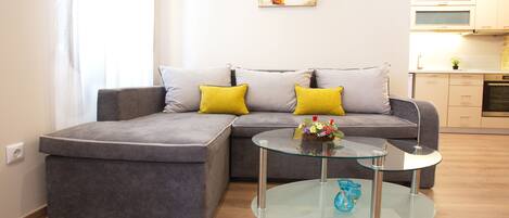 Una sala de estar moderna con un sofá seccional gris, dos cojines amarillos y una mesa de centro de vidrio.