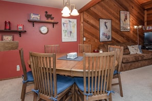 A dining area with a wooden table and chairs, a red wall, and various decorations including a wine map and a poster.