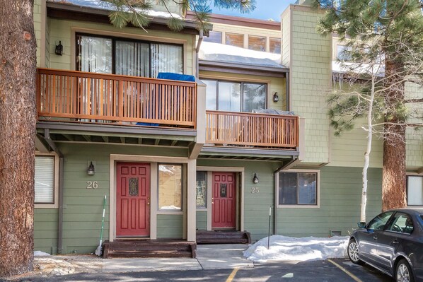 A two-story building with a green facade, numbered doors, and a wooden balcony.