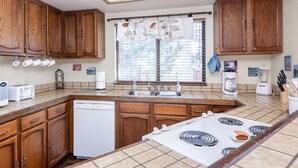A kitchen with wooden cabinets, a dishwasher, a stove, and a window with blinds.