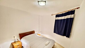 A bedroom with a bed, a nightstand, a lamp, a window with curtains, and a ceiling light.