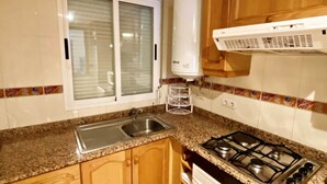 A kitchen with wooden cabinets, a gas stove, a sink, and a window with blinds.