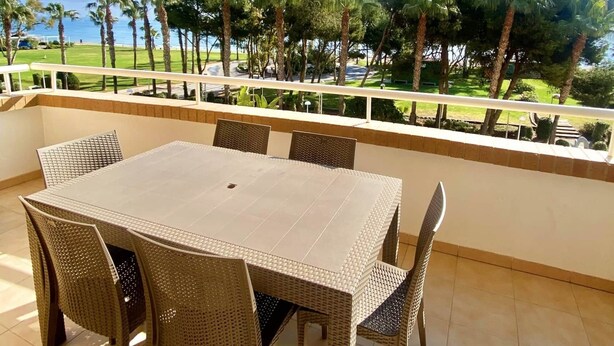 A covered outdoor dining area with a table and chairs, overlooking a landscaped garden and a body of water.