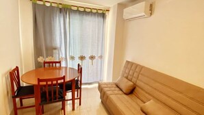 A living room with a sofa, a dining table with chairs, a ceiling light fixture, and a window with curtains.