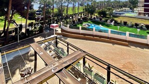 A pool area with a view of the ocean, surrounded by palm trees and a building with multiple floors.