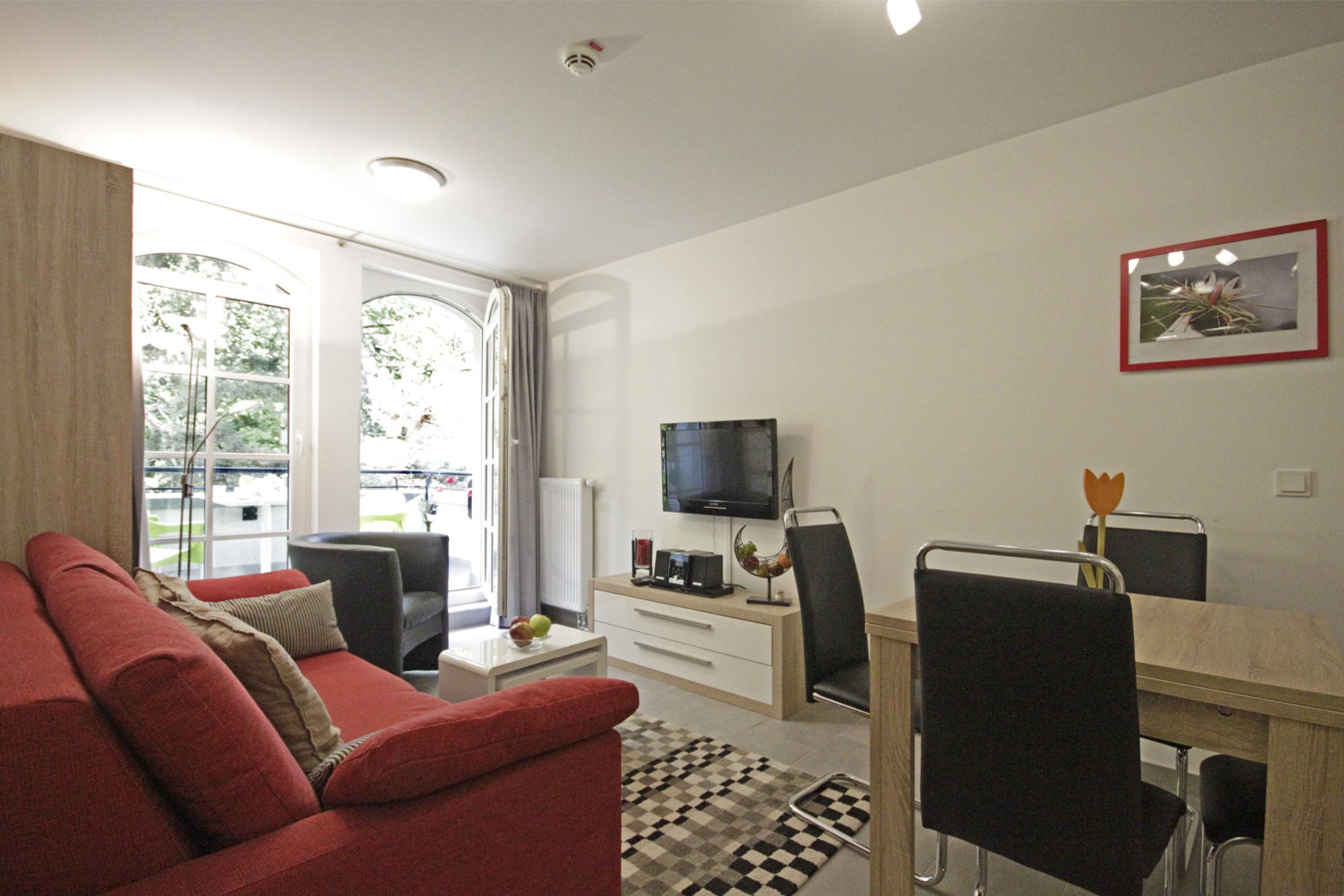 Una sala de estar moderna con un sofá rojo, una mesa de comedor con sillas, un televisor y una ventana con cortinas.