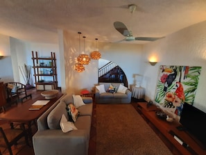 A living room with a sofa, a dining table, a TV, and a ceiling fan.