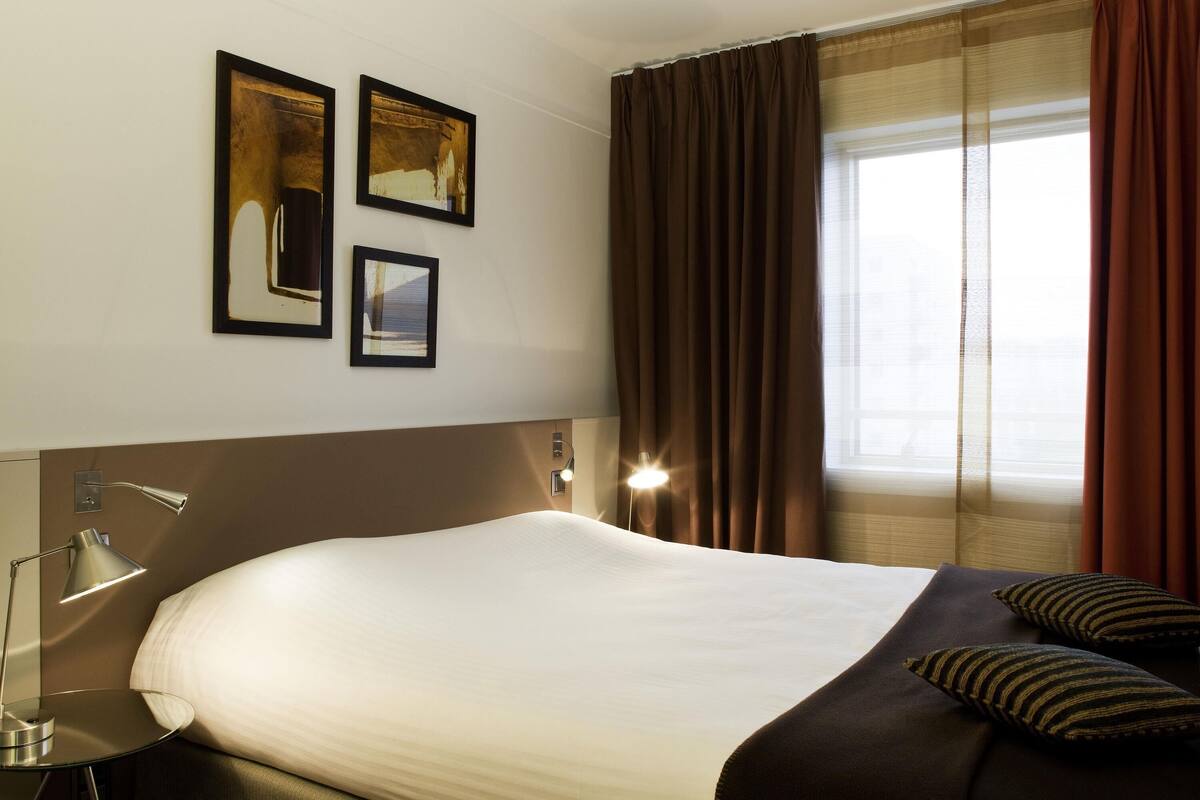 Habitación de hotel con una cama grande, una mesita de noche con lámpara y dos cuadros en la pared.