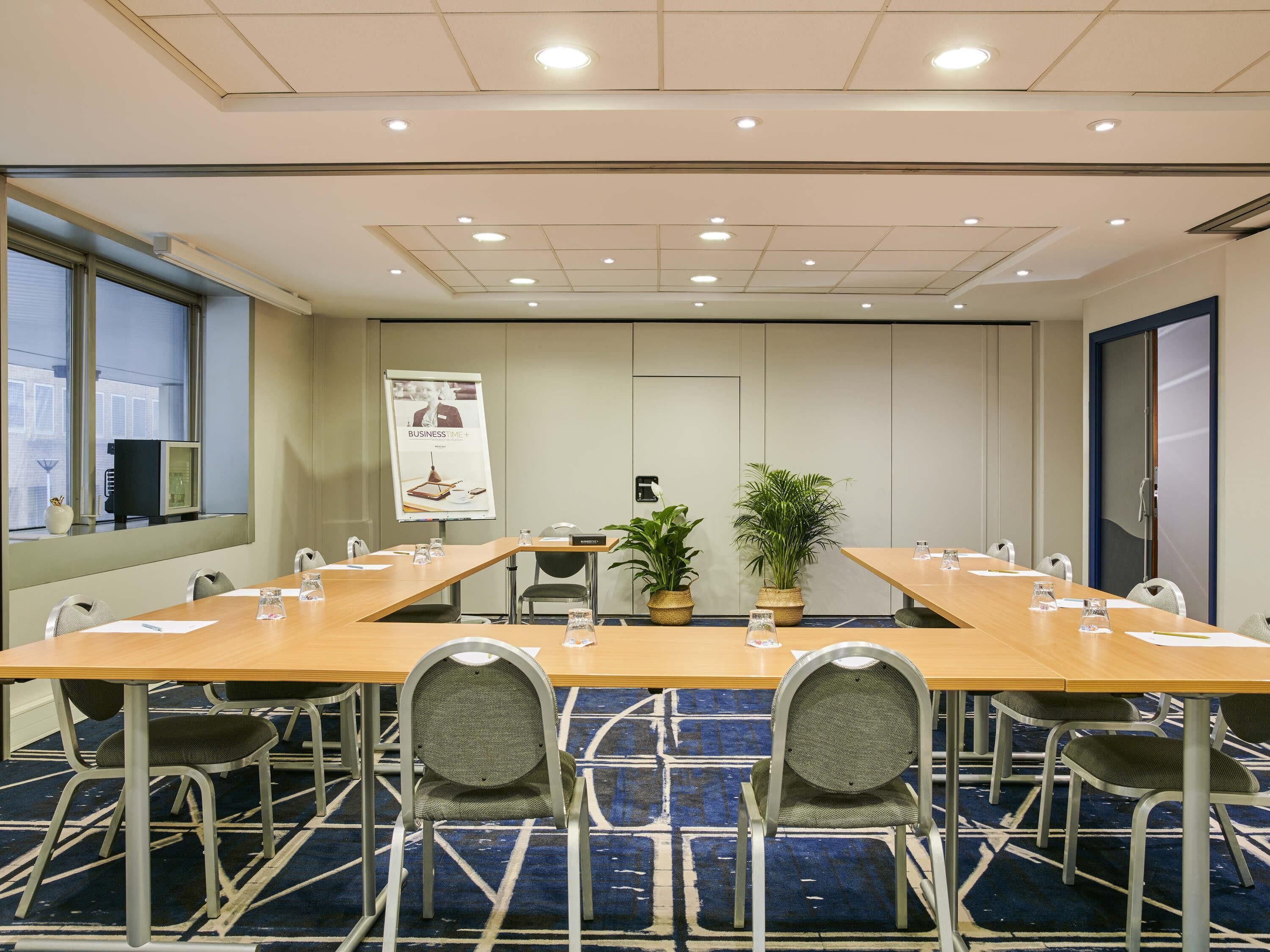 A conference room with a long table, chairs, a potted plant, and a poster on the wall.