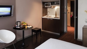 Une chambre d’hôtel compacte comprenant un coin cuisine, un téléviseur à écran plat, une petite table à manger avec une chaise et un lit.