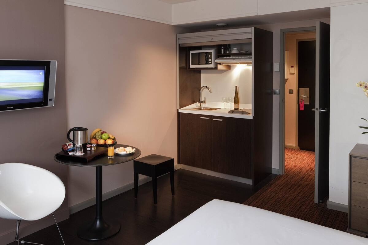 Una habitación de hotel compacta con kitchenette, un televisor de pantalla plana, una pequeña mesa de comedor con una silla y una cama.