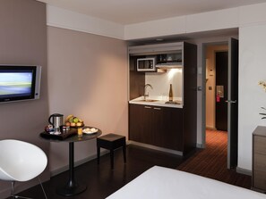 Una habitación de hotel compacta con kitchenette, un televisor de pantalla plana, una pequeña mesa de comedor con una silla y una cama.
