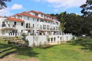 Un immeuble à plusieurs étages doté de balcons, un espace jardin avec des arbres et un ciel dégagé.