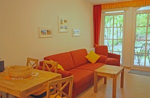 A living room with a sofa, chairs, a table, and a window with a view of greenery. - Haus Meeresblick FeWo Abendrot A 1.31 Ref. 132364 - FeWo Abendrot A 1.31 Ref. (Baabe)