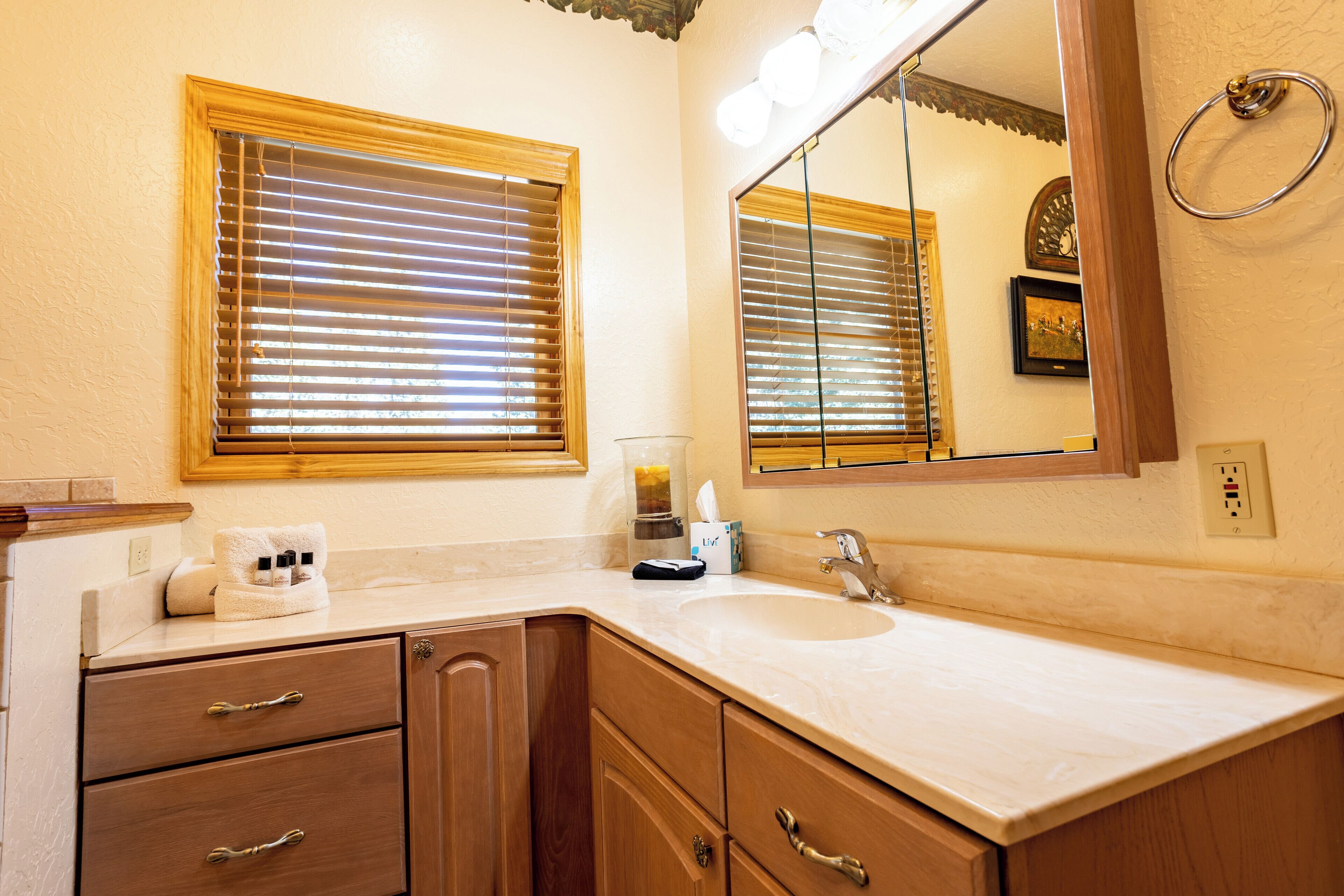 A bathroom with a sink, mirror, wooden cabinets, and a window with blinds.