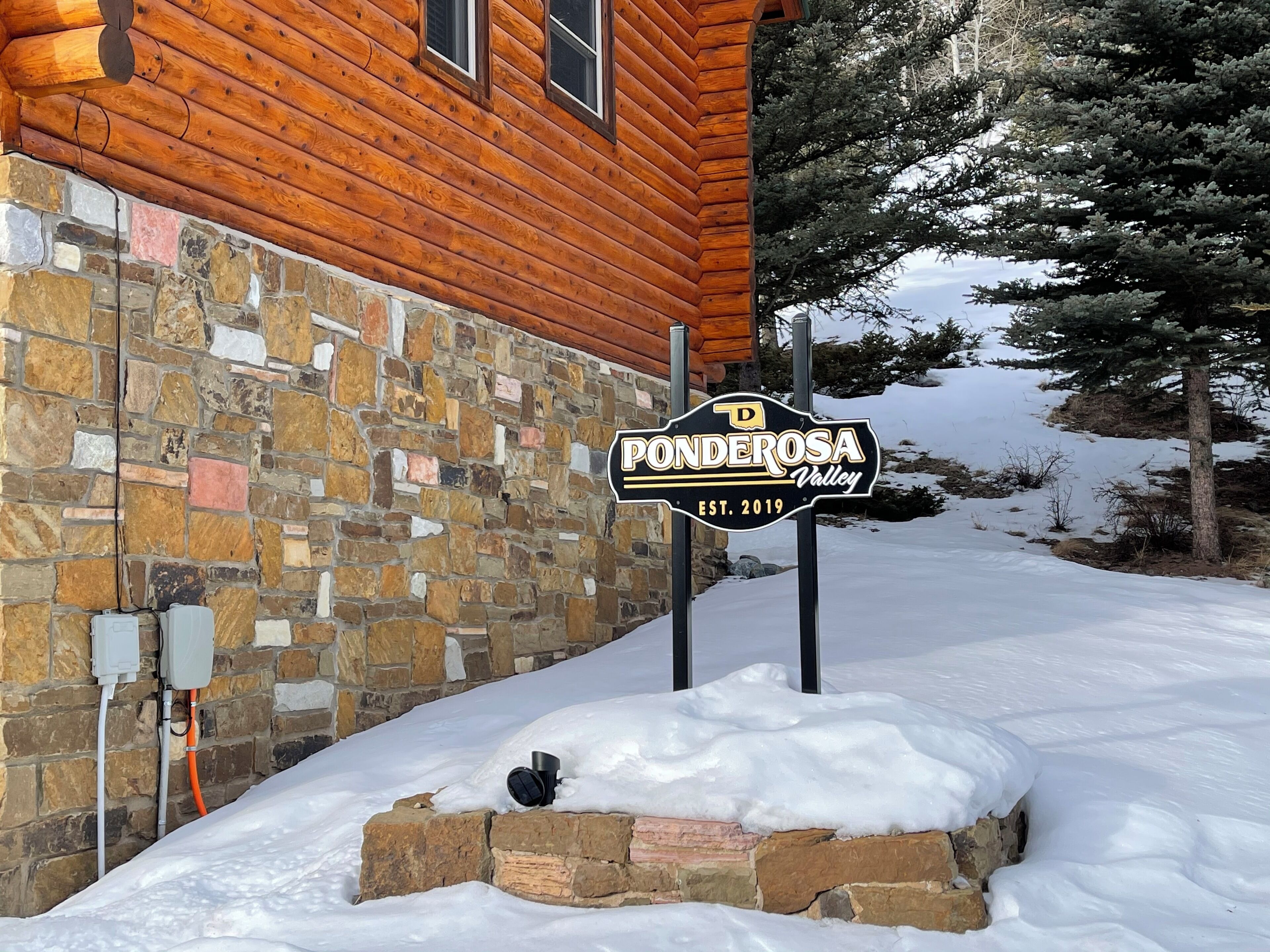 Un mur de pierres, une cabane en bois et une pancarte indiquant « Ponderosa Valley ».