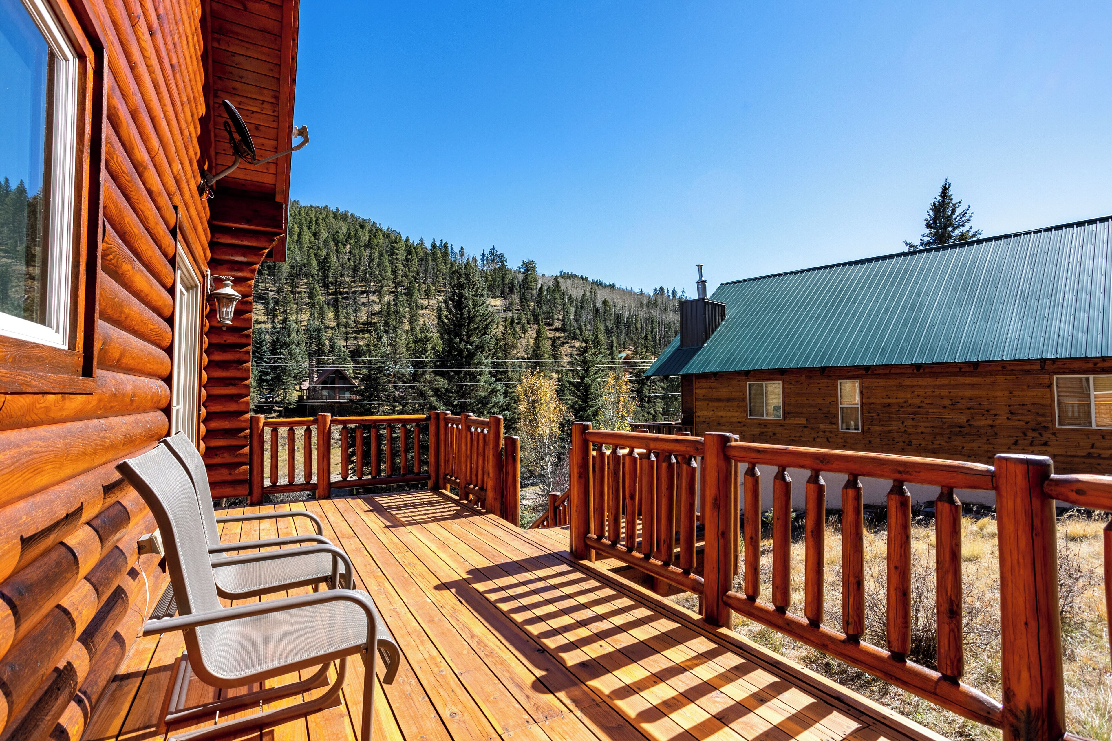 Une terrasse en bois avec des chaises, une rambarde et une vue sur une montagne boisée.