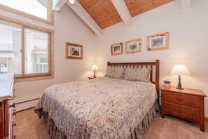 A bedroom with a large bed, two bedside tables with lamps, a wooden headboard, and three framed pictures on the wall. - Mammoth Creek #52 (Mammoth Lakes)