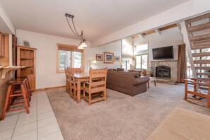 A cozy living room with a fireplace, wooden furniture, and large windows. - Mammoth Creek #52 (Mammoth Lakes)
