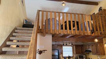 A staircase with wooden railings leading to a lofted area, a kitchen with wooden cabinets, a refrigerator, and a window with blinds.