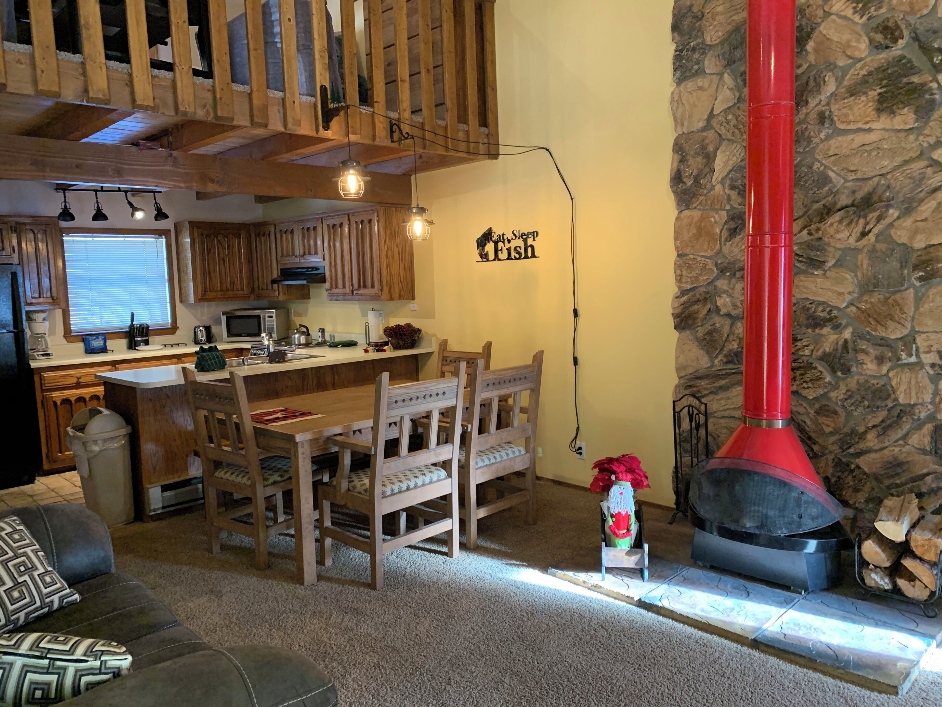 A cozy living room with a wooden dining table, chairs, a fireplace, and a kitchen area with wooden cabinets and a stone wall.