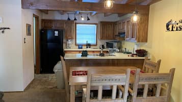 A kitchen with wooden cabinets, a black refrigerator, a dining table with chairs, and pendant lights.