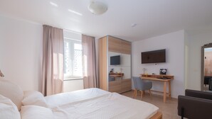 A hotel room with a large bed, a desk with a chair, a TV, and a wardrobe.