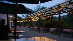 An outdoor patio area with tables and chairs, string lights, and a pergola structure.