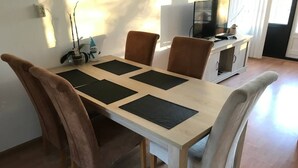 A dining table with four chairs, a TV, and a cabinet in a room with wooden flooring.