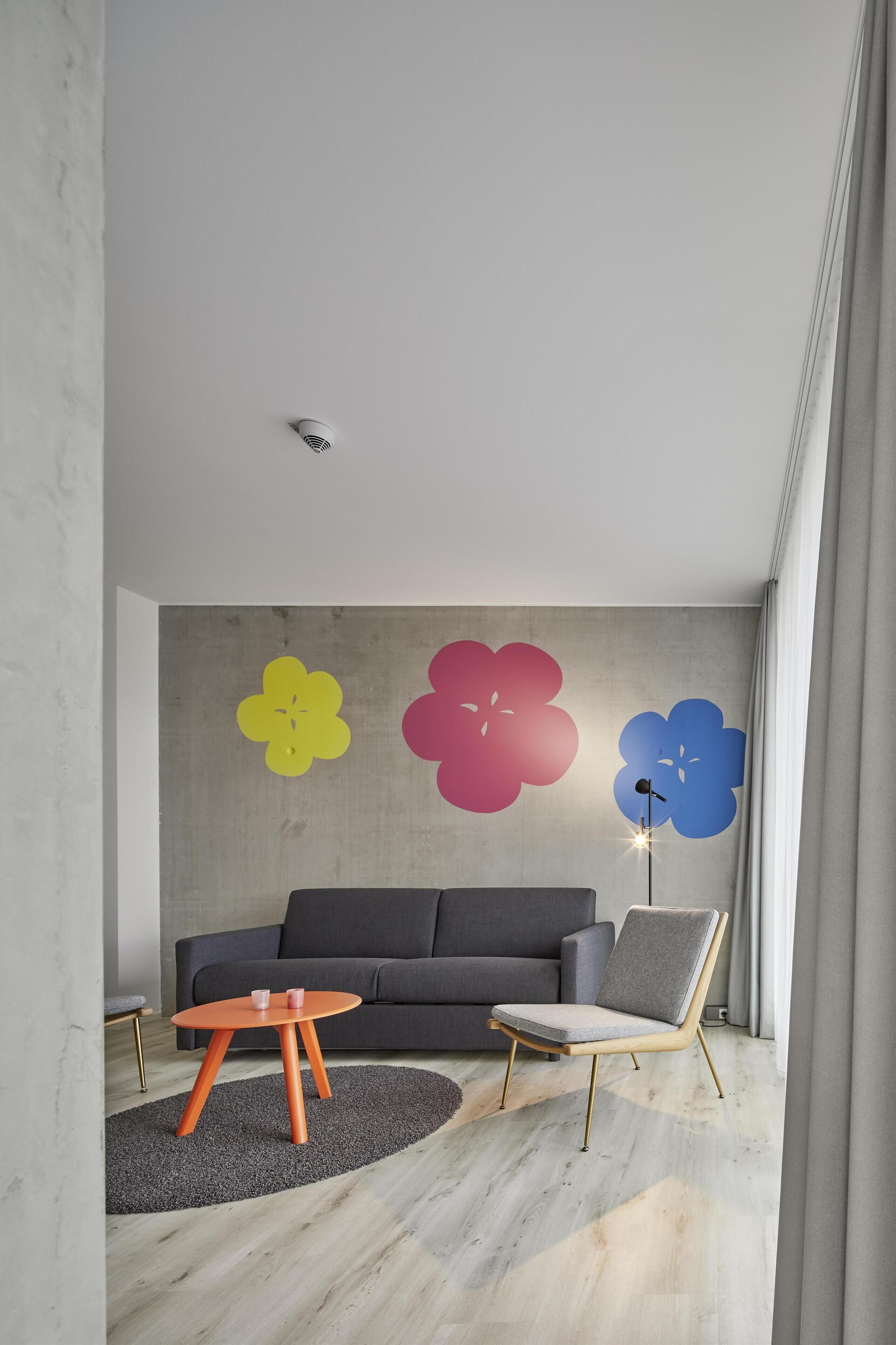 Una sala de estar moderna con un sofá gris, una mesa redonda naranja y una lámpara de pie.