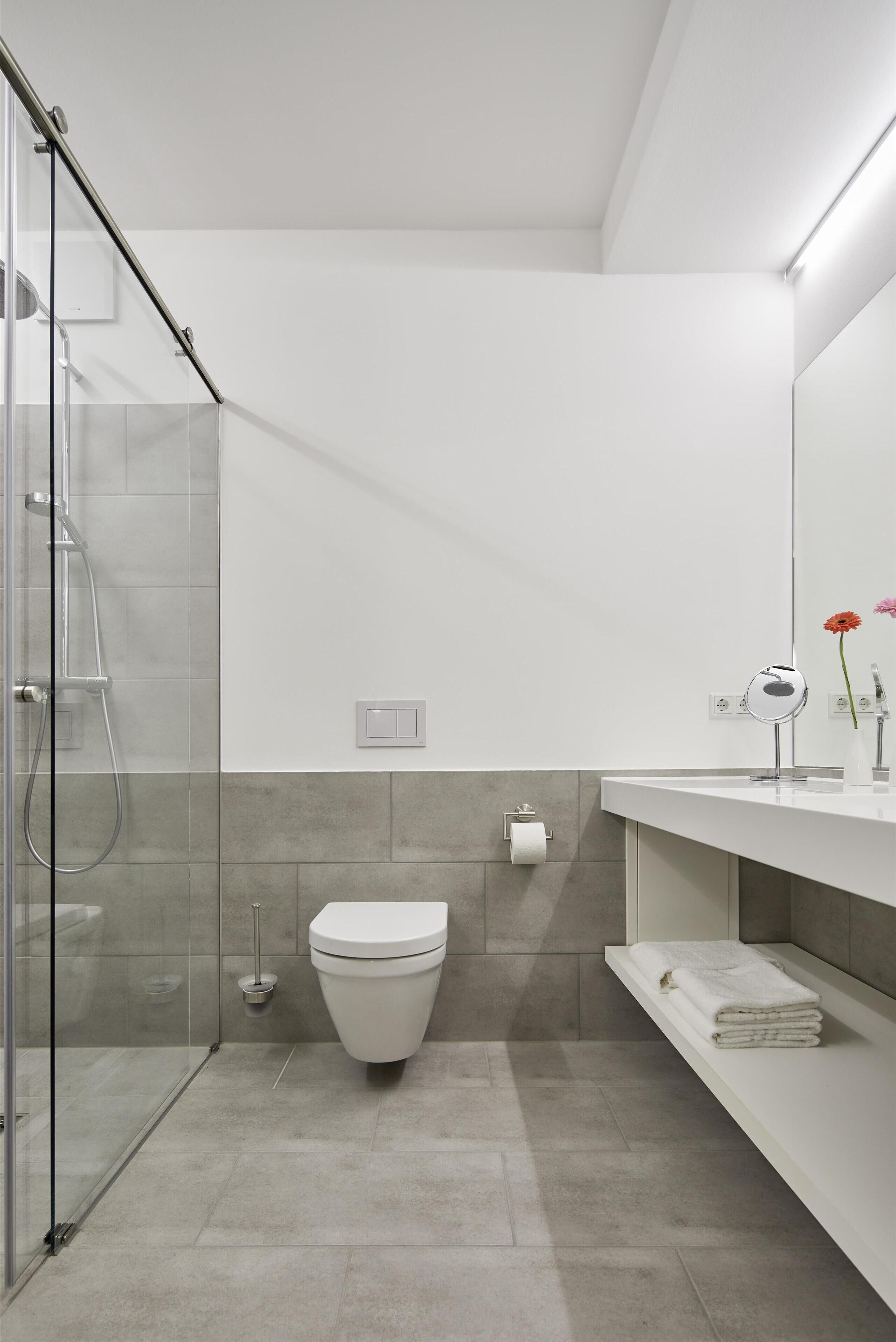 Un baño moderno con cabina de ducha de vidrio, inodoro blanco y tocador con espejo y toallero.
