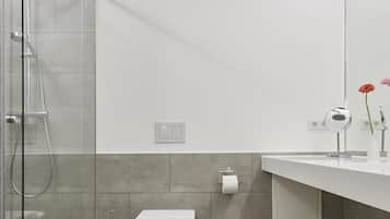 Un baño moderno con cabina de ducha de vidrio, inodoro blanco y tocador con espejo y toallero.