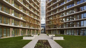 A modern multi-story building with a central courtyard, featuring balconies with green plants and a pathway leading to the entrance. - Flowers Hotel Essen (Essen)