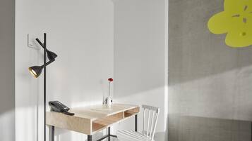Un espace de bureau moderne avec un bureau en bois, une chaise blanche, une lampe de bureau noire et un téléphone fixé au mur.