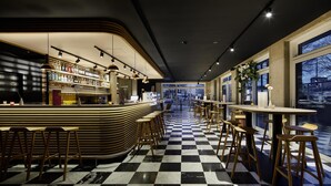 A bar area with a checkered floor, bar stools, and a counter with bottles and glasses. - Flowers Hotel Essen (Essen)