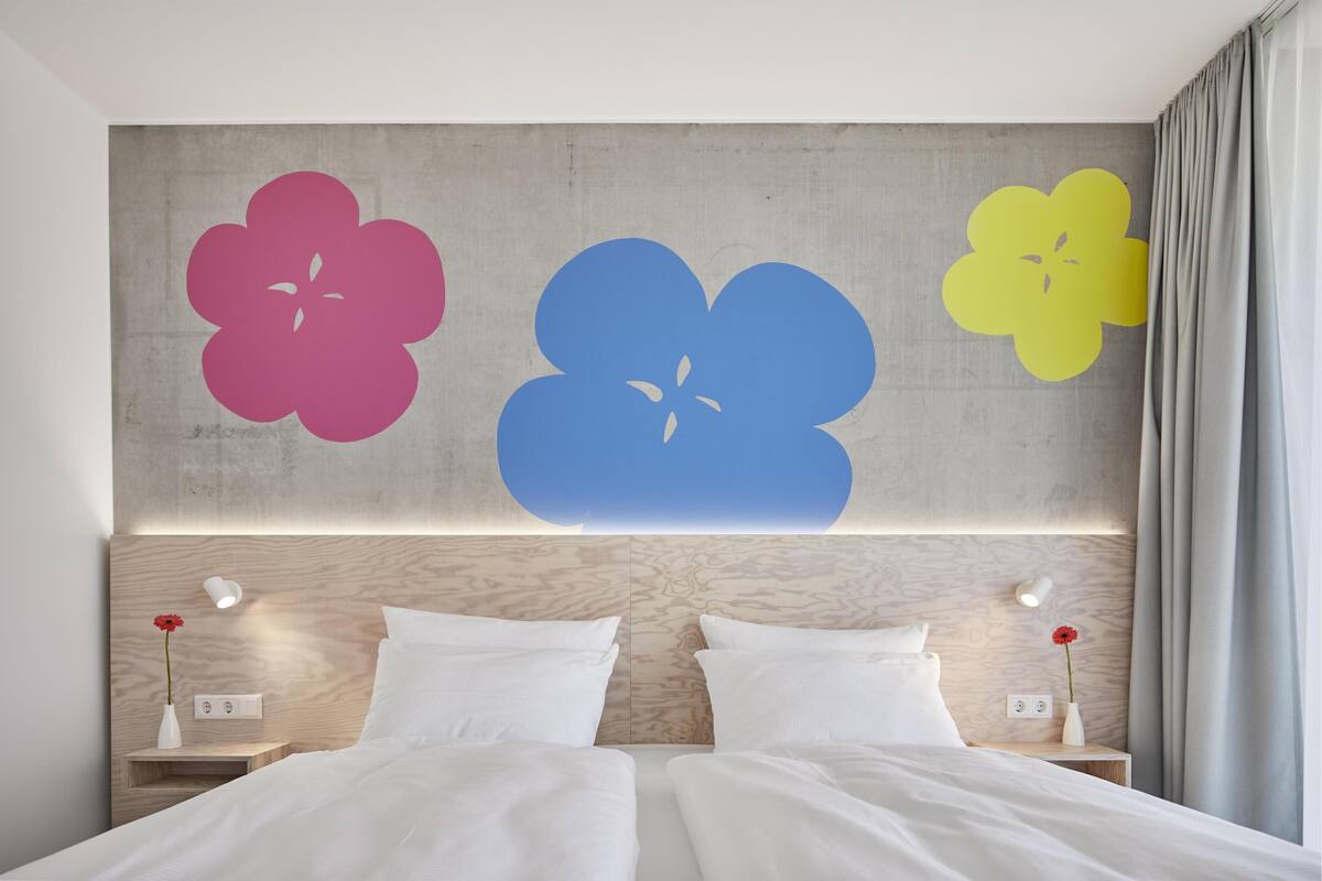 Ein Doppelbett mit weißen Bettwäsche, zwei Nachttische mit Lampen und eine Wand mit drei großen Blumenmotiven.