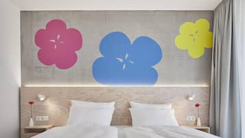 A double bed with white linens, two bedside tables with lamps, and a wall with three large flower decals.