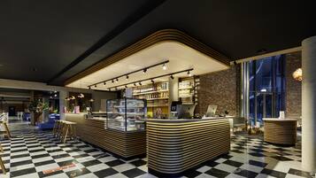 A modern lobby with a checkered floor, a central counter with a display case, seating areas, and a brick wall.