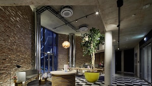 A modern lobby with a checkered floor, exposed brick walls, and a large potted plant. - Flowers Hotel Essen (Essen)